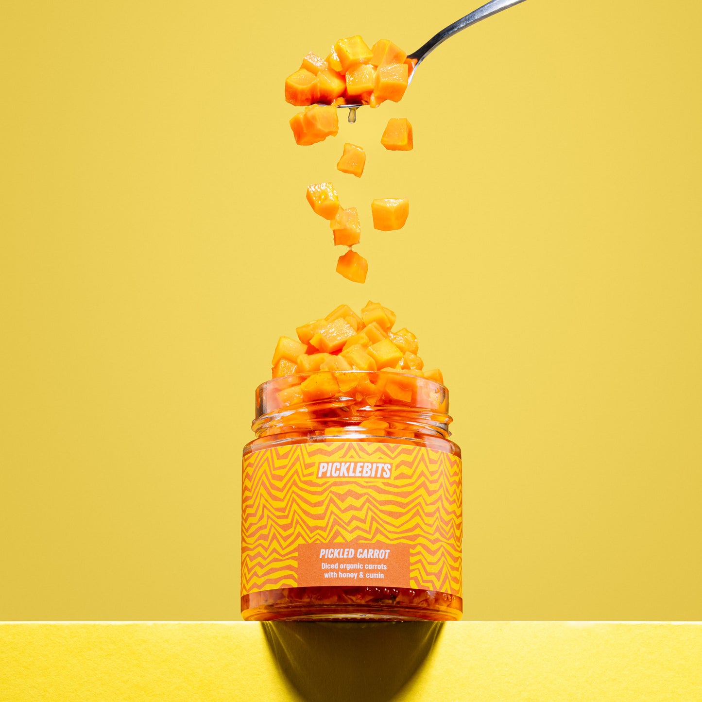 Jar of organic pickled carrot chopped tumbling on yellow background