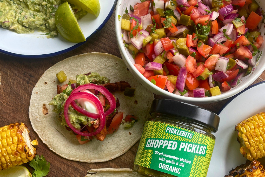 A table spread of Pickle de Gallo with tacos and a jar of Chopped Dill Pickles