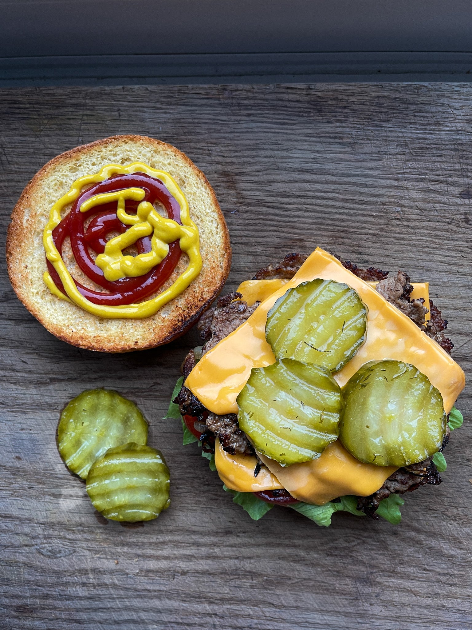 Open burger with organic crinkle cut pickles and condiments on a wooden surface