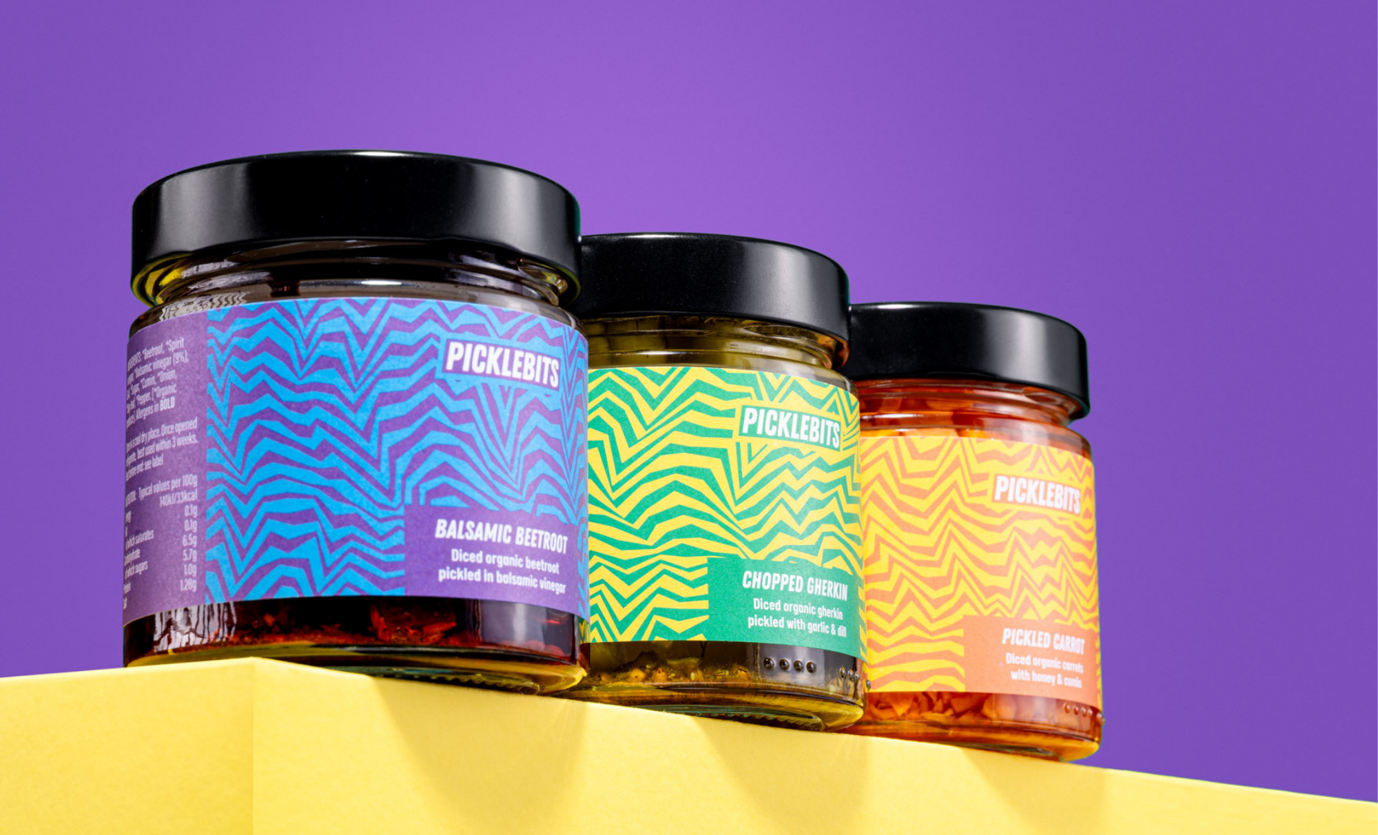 Three jars of PICKLEBITS organic pickles on a purple background. Perfect for burgers and pickle sandwiches