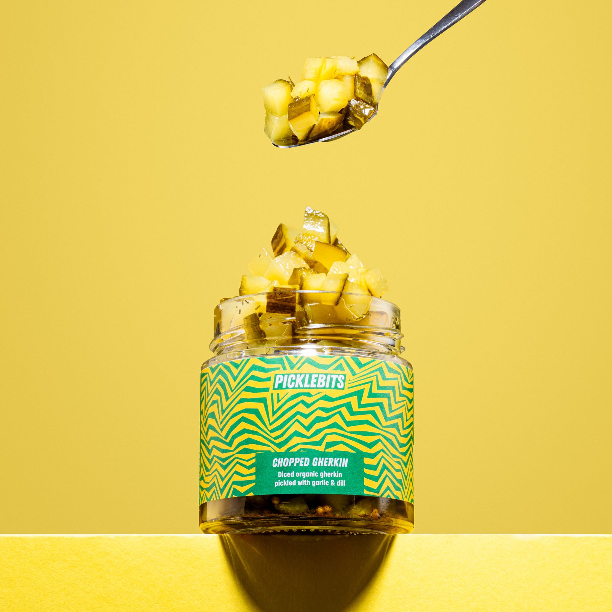 Jar of organic pickle gherkin chopped kosher dill pickles spoon on yellow background