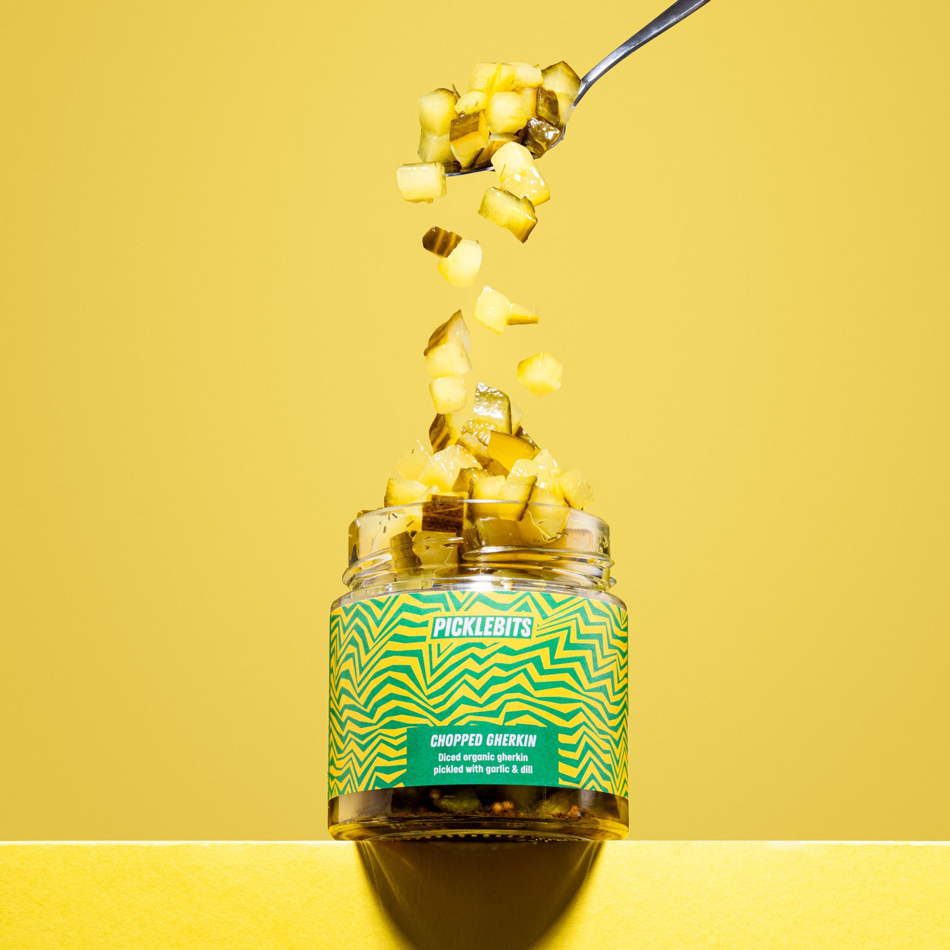 Jar of organic pickle gherkin chopped kosher dill pickles tumbling on yellow background