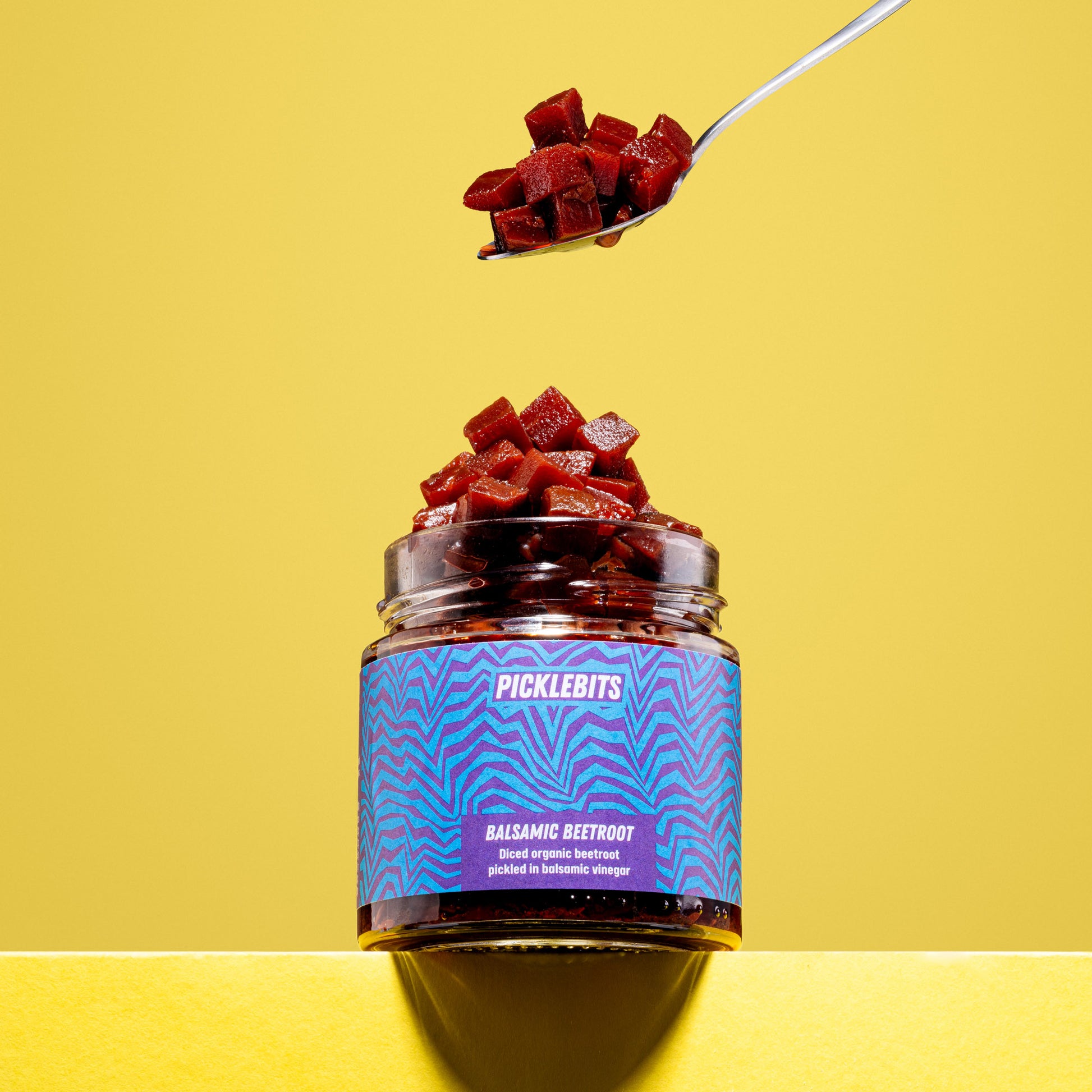 Jar of organic pickled beetroot beets on a spoon with yellow background
