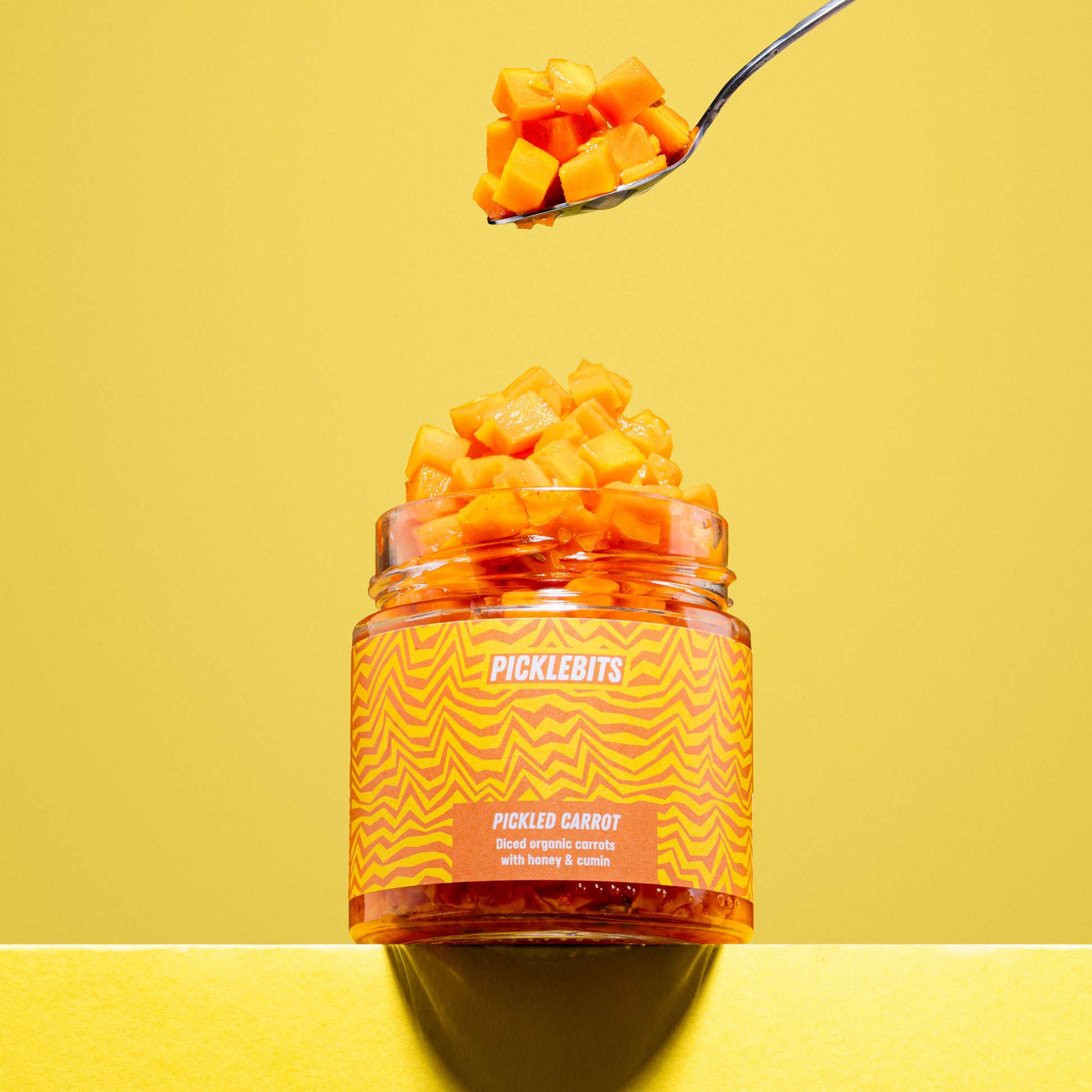 Jar of organic pickled carrot chopped with spoon on yellow background