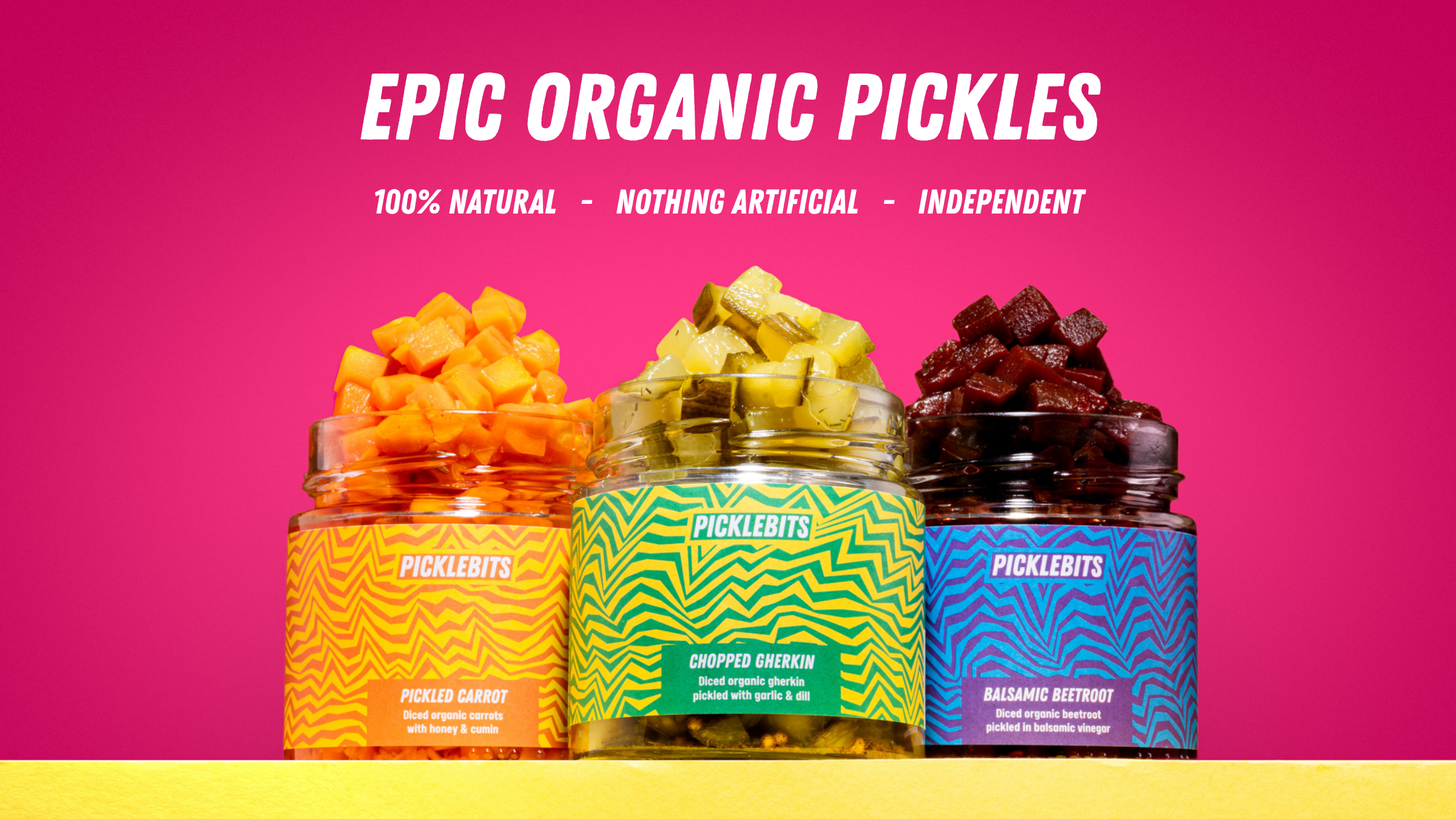 Three jars of pickles with colorful labels on a pink background, featuring the brand 'PICKLEBITS'.